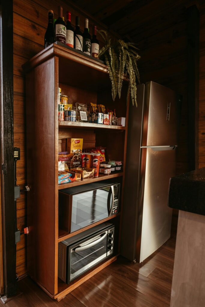 pexels-photo-19737854-19737854 Wooden shelf with snacks and wine, next to modern fridge, in a rustic kitchen setting.