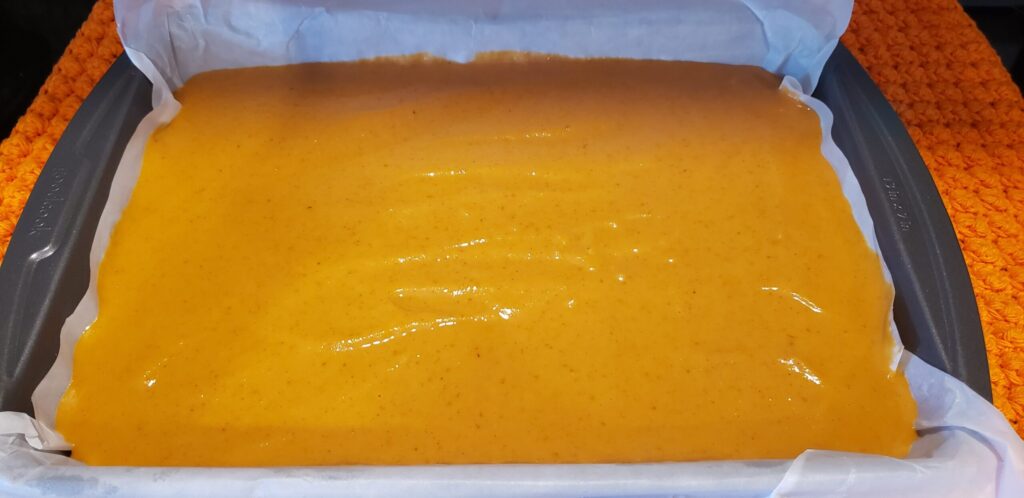 Pumpkin pie filling poured over oat crust in a parchment-lined pan, ready to bake